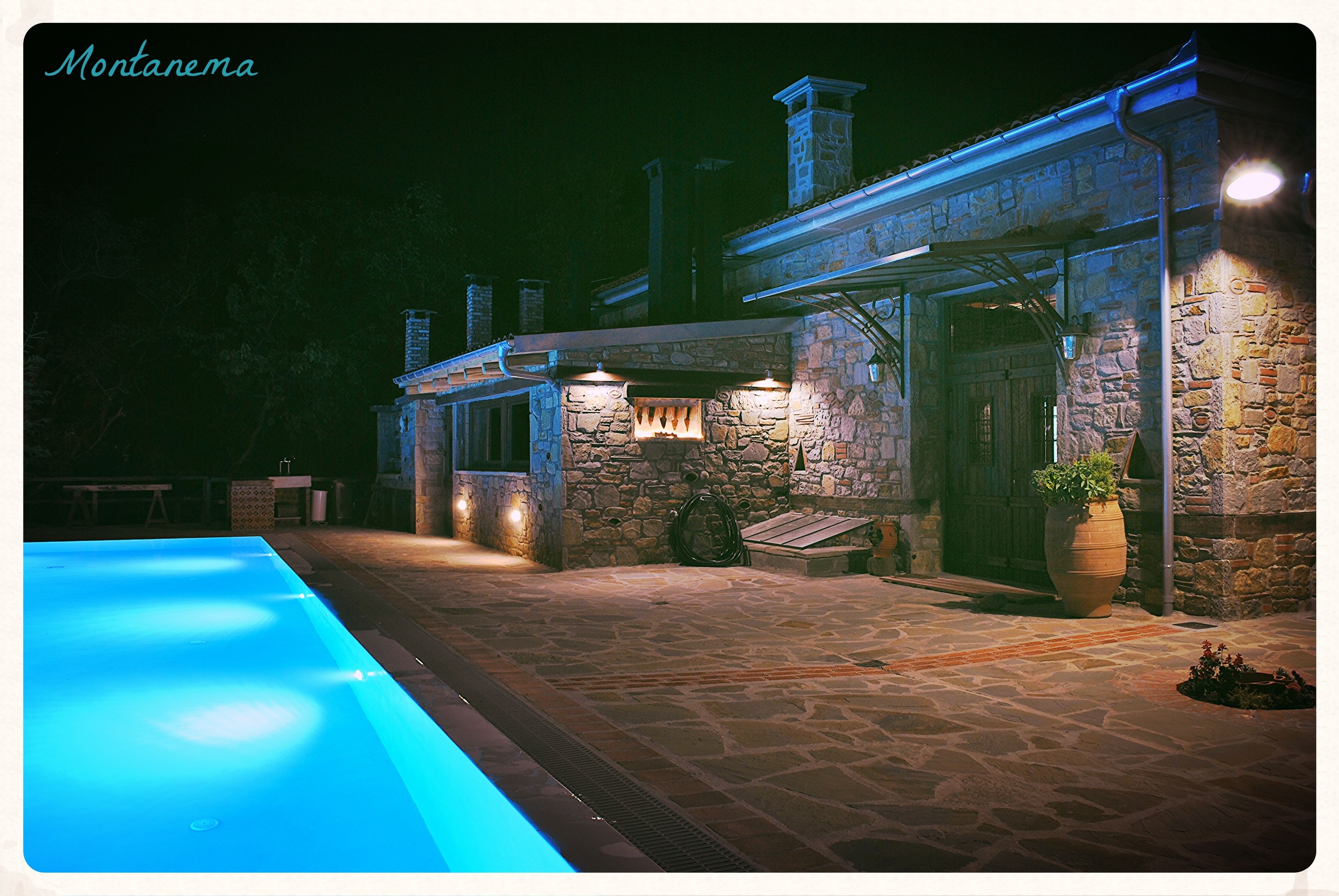 Un edificio de piedra con piscina, zona de estar al aire libre y un patio bien iluminado.