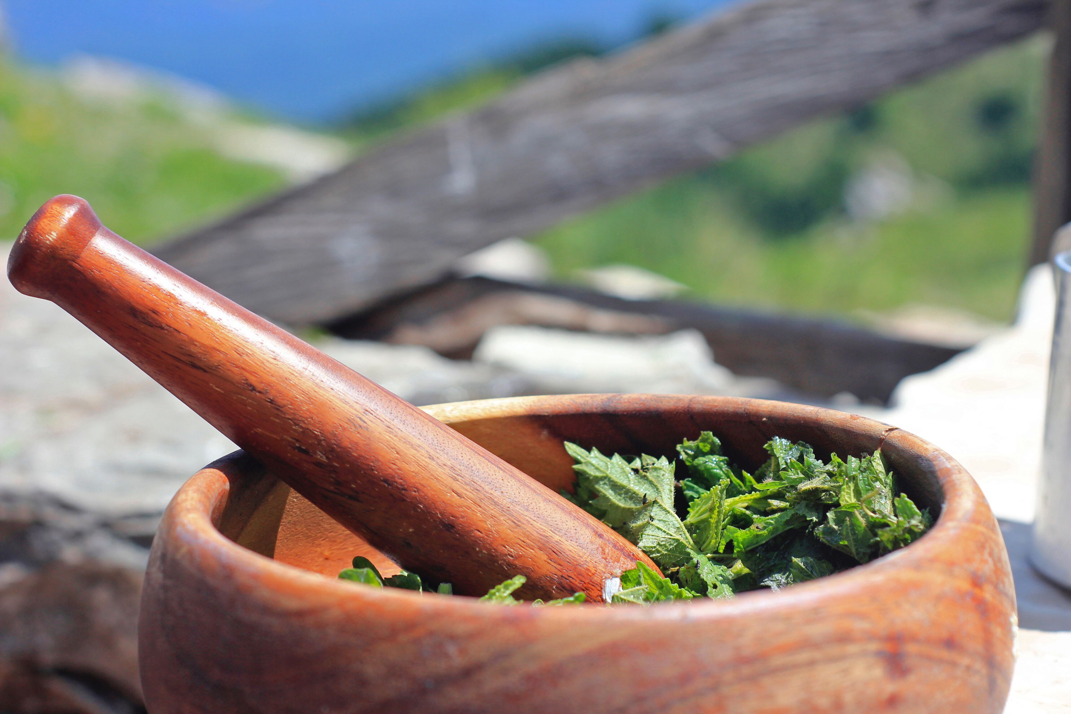 A wooden mortar with a pestle containing chopped herbs.