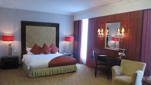 A hotel room with a large bed, two bedside lamps, a desk with a chair, a mirror, and a patterned carpet. - The Mark's Lodge (Sandakan)