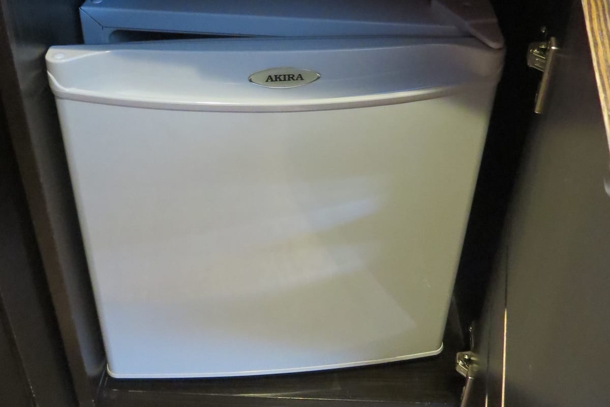 A compact refrigerator with a brand label, situated in a kitchen with a dark countertop and a drawer above.