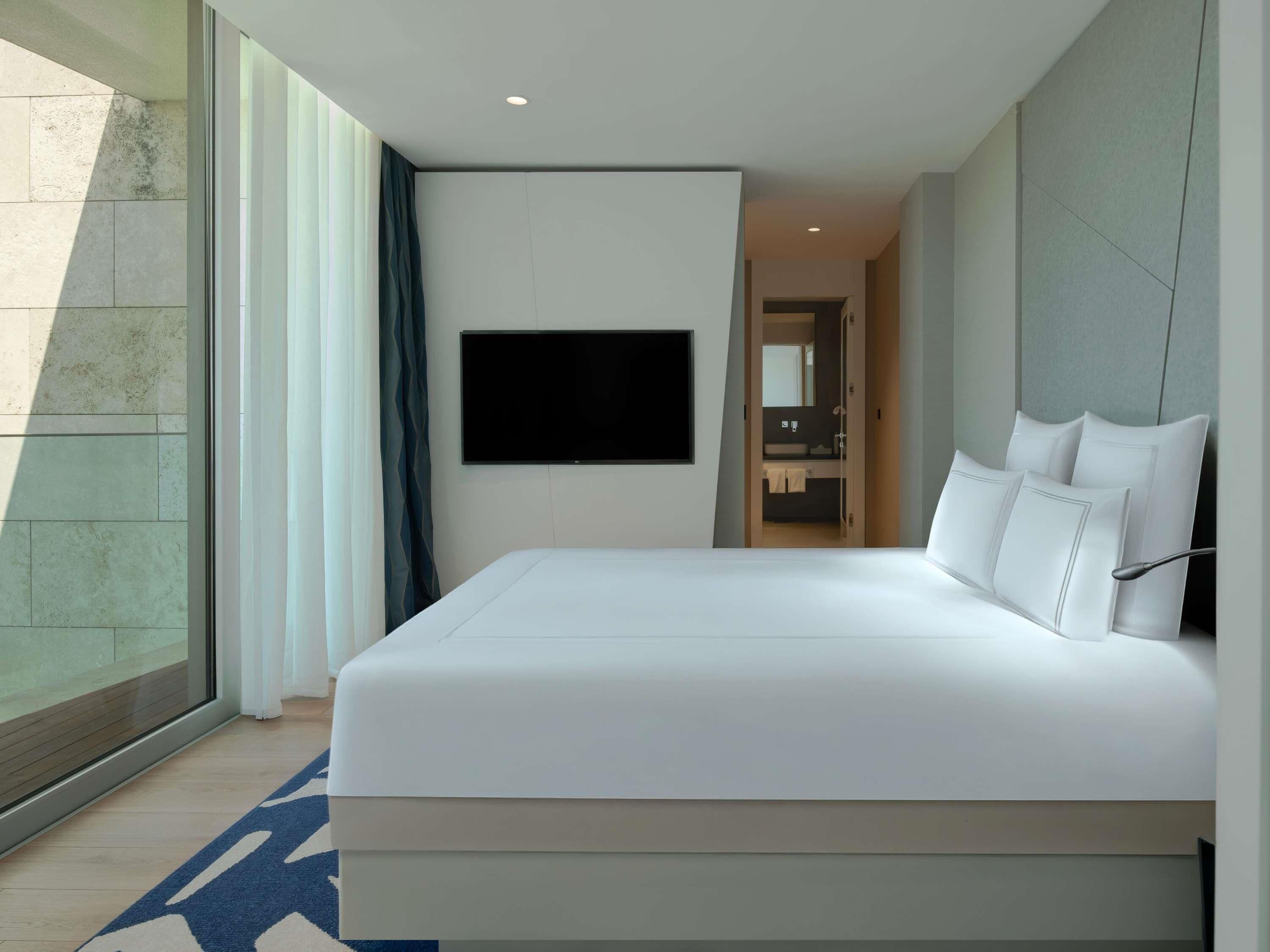 Een moderne hotelkamer met een groot bed, een flatscreen televisie aan de muur en een badkamer door een open deur zichtbaar.
