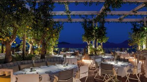 Un espacio de comedor al aire libre con mesas y sillas, rodeado de árboles y vistas a las montañas.