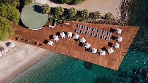 Vista aérea de un complejo turístico frente a la playa, con una terraza de madera, tumbonas y sombrillas dispuestas para los huéspedes.