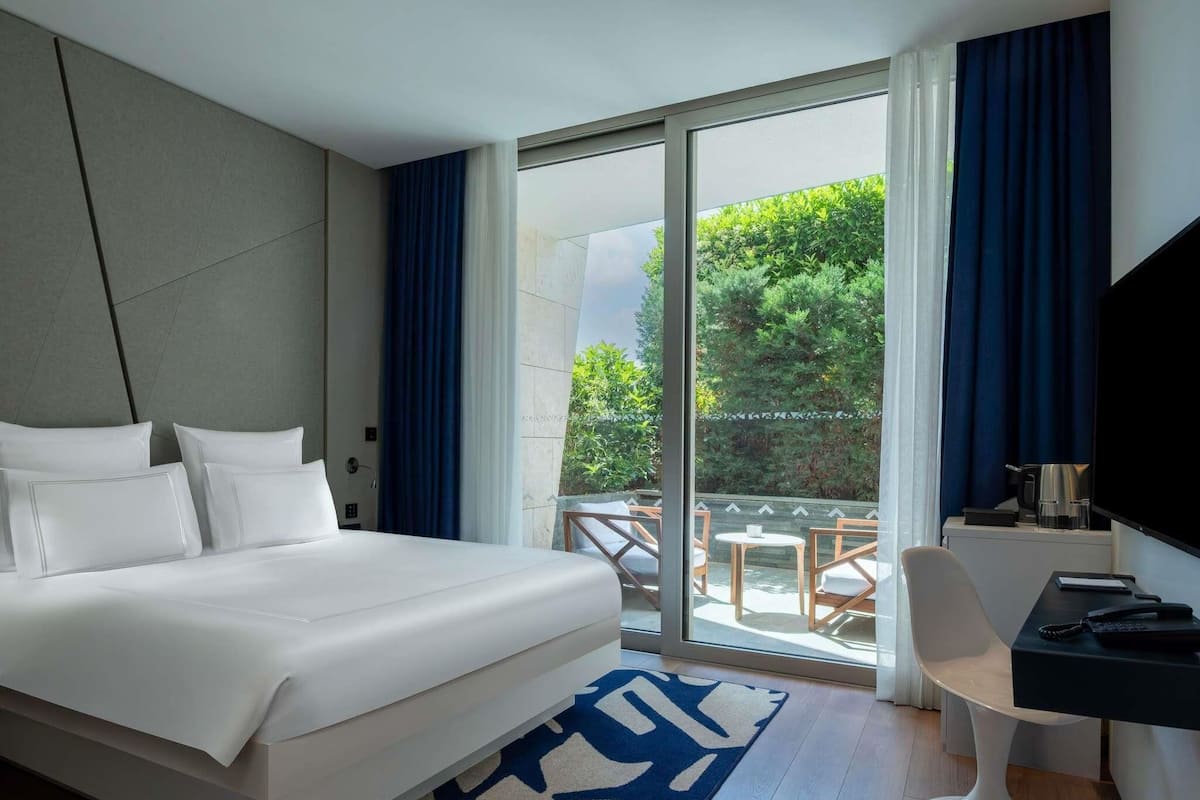 A hotel room with a large bed, a desk with a chair, and a view of the outdoors.