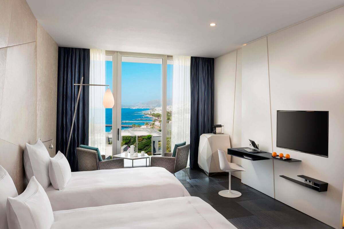 Una habitación de hotel moderna con un ventanal grande, una cama, un escritorio, una silla y un televisor de pantalla plana.