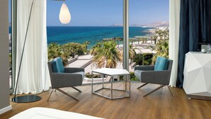 Una habitación moderna con un ventanal grande, dos sillones grises, una mesita pequeña y una lámpara de pie.