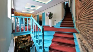 A staircase with red carpet and blue railings, leading to a lower level with tables and chairs. - City Inn - Boutique Hotel Tbilisi (Tbilisi)