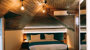 A bedroom with a sloped ceiling, wooden beams, a bed with white bedding, a nightstand, and a wall-mounted air conditioner. - City Inn - Boutique Hotel Tbilisi (Tbilisi)