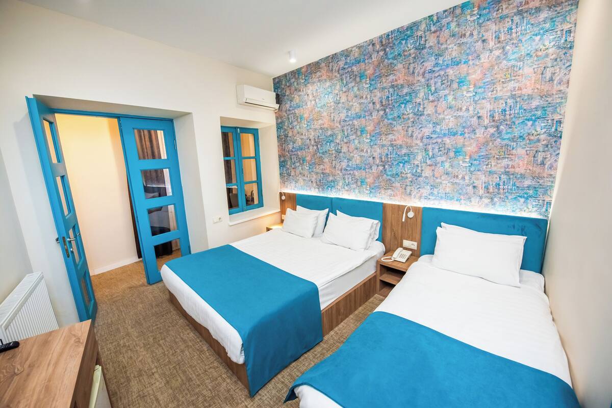 A hotel room with two beds, a large abstract painting on the wall, and a blue door.