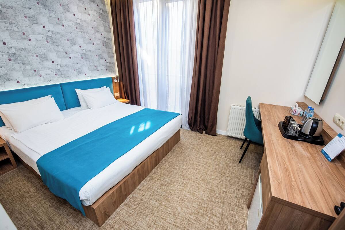 A hotel room with a bed, a desk, a chair, and a window with curtains.