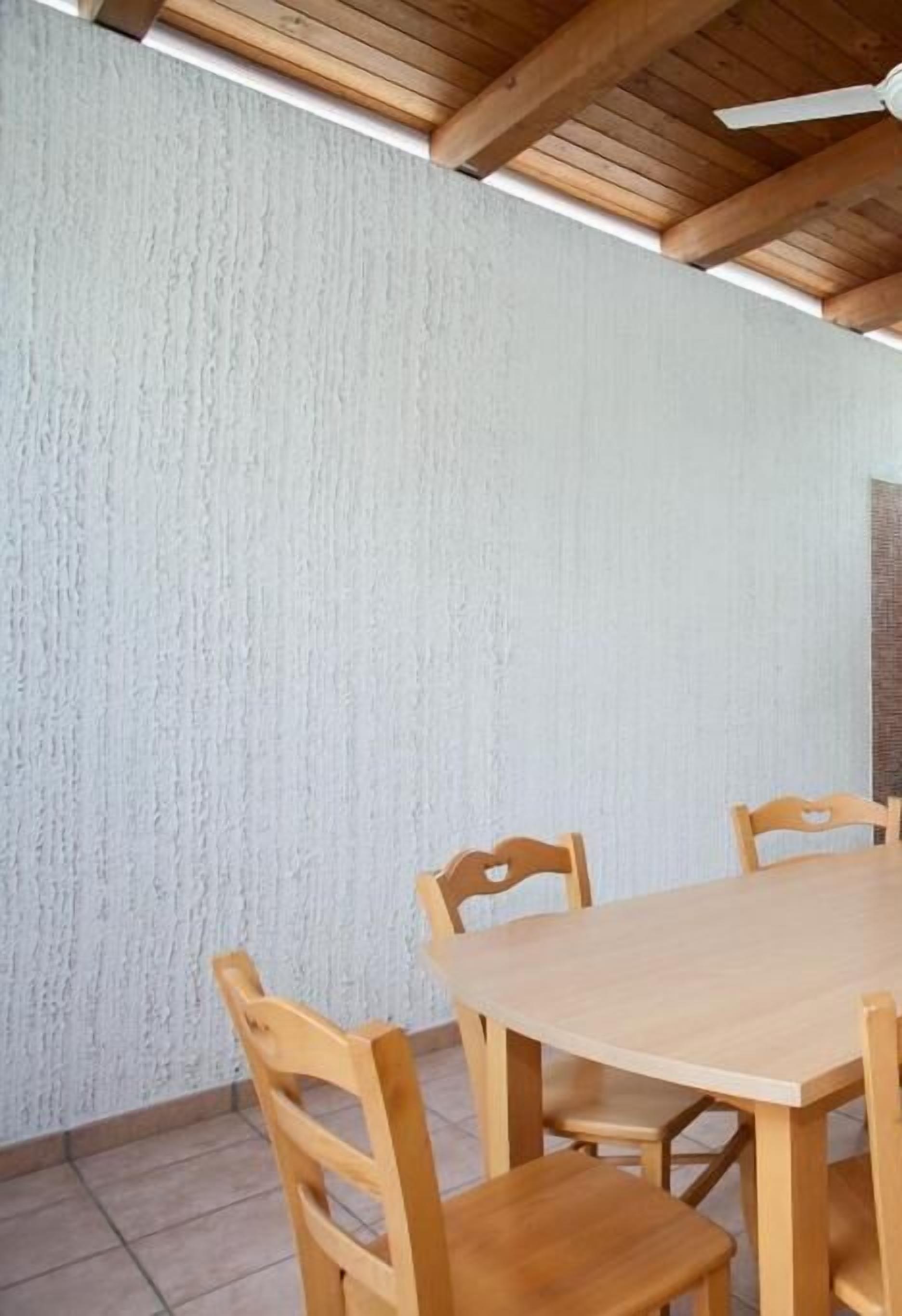 Un comedor con mesa y sillas de madera, pared con textura y ventilador de techo.