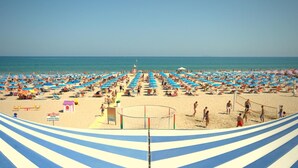 A beach with numerous umbrellas and sun loungers, a volleyball net, and a lifeguard tower. - Villaggio Albatros (Lesina)