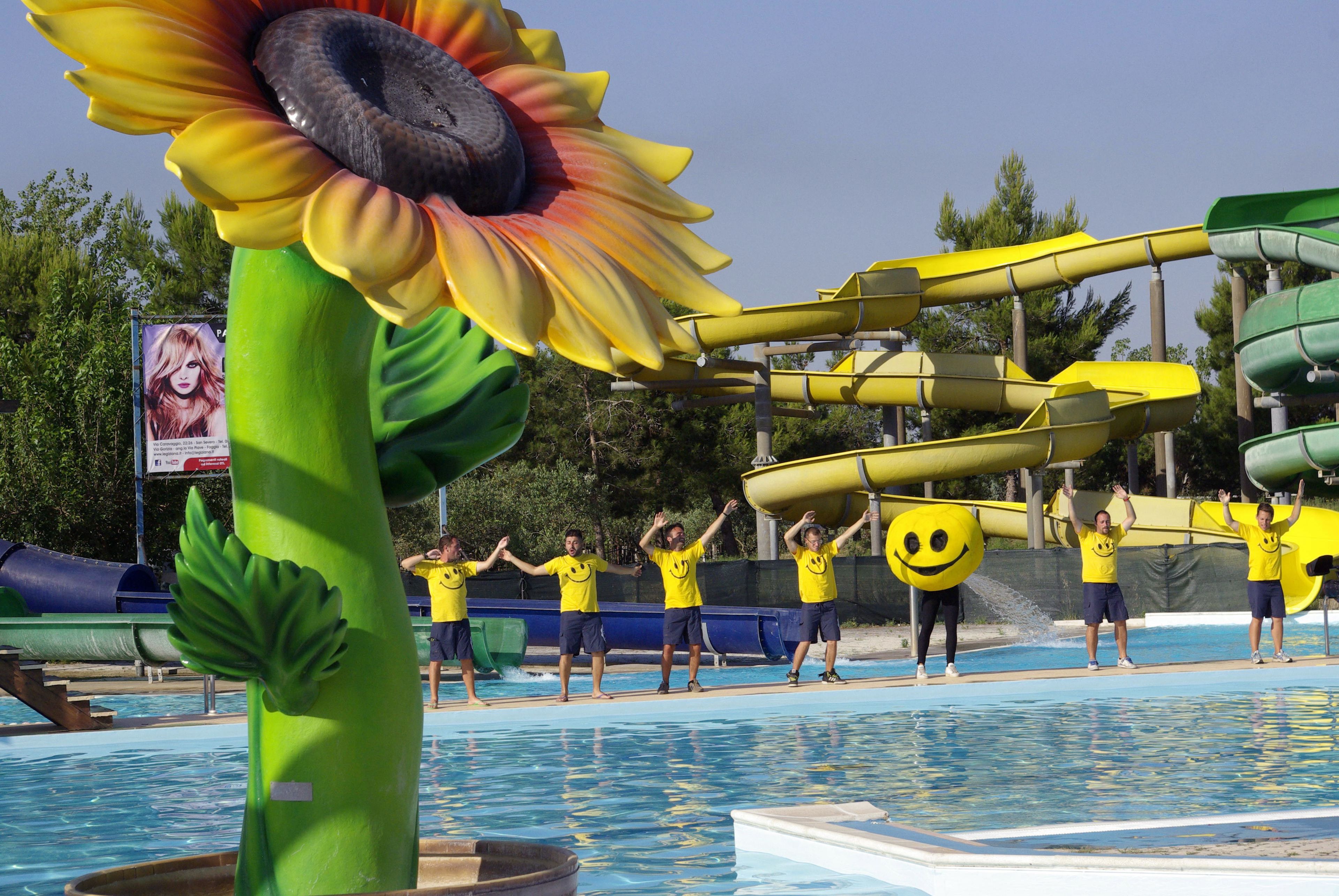 A pool area with a large sunflower decoration, a water slide, and people in yellow shirts.