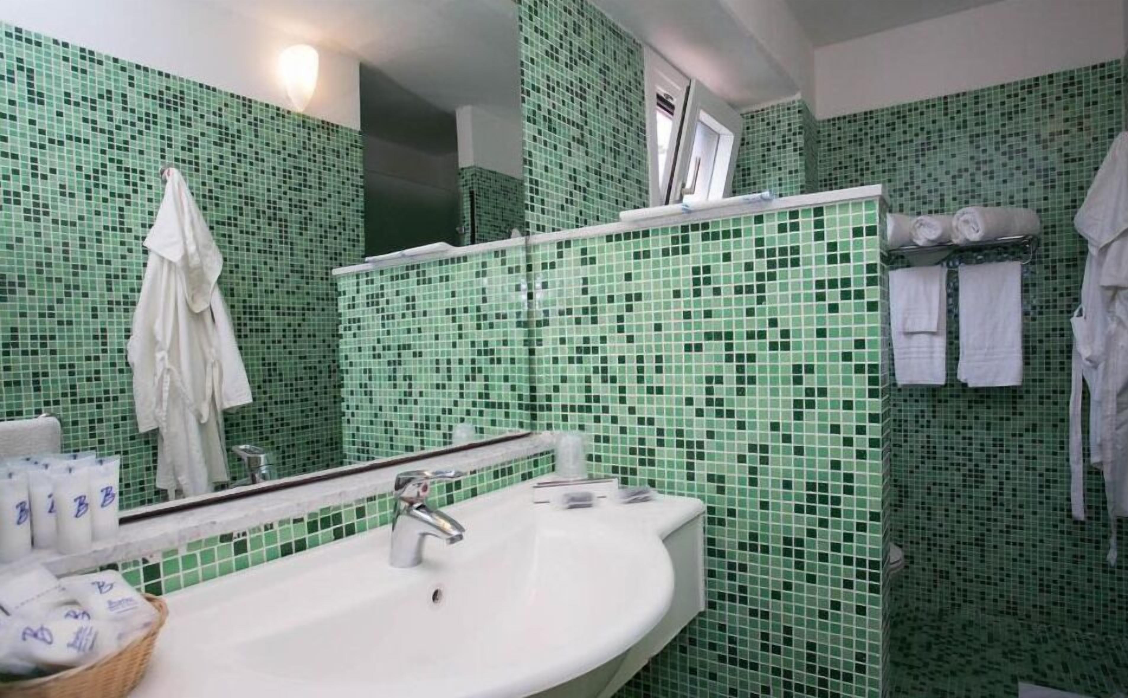 Une salle de bain avec des carreaux de mosaïque verts, un lavabo blanc et un miroir.