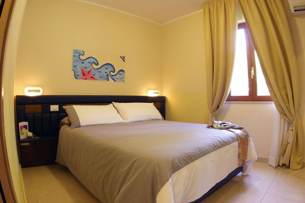 A bedroom with a bed, nightstands, a wall art piece, and a window with curtains.