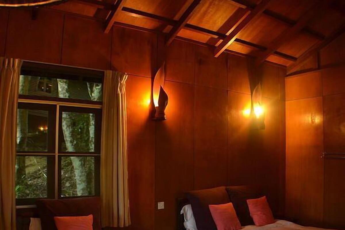 A room with two beds, wooden walls, and a window with curtains.