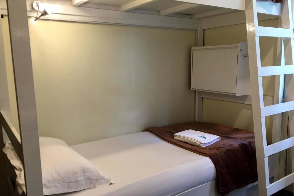 A bunk bed with a white mattress and a brown blanket. There is a small white cabinet above the bed.