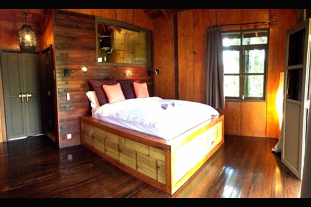 A wooden cabin bedroom with a large bed, a wooden wardrobe, and a window with curtains.