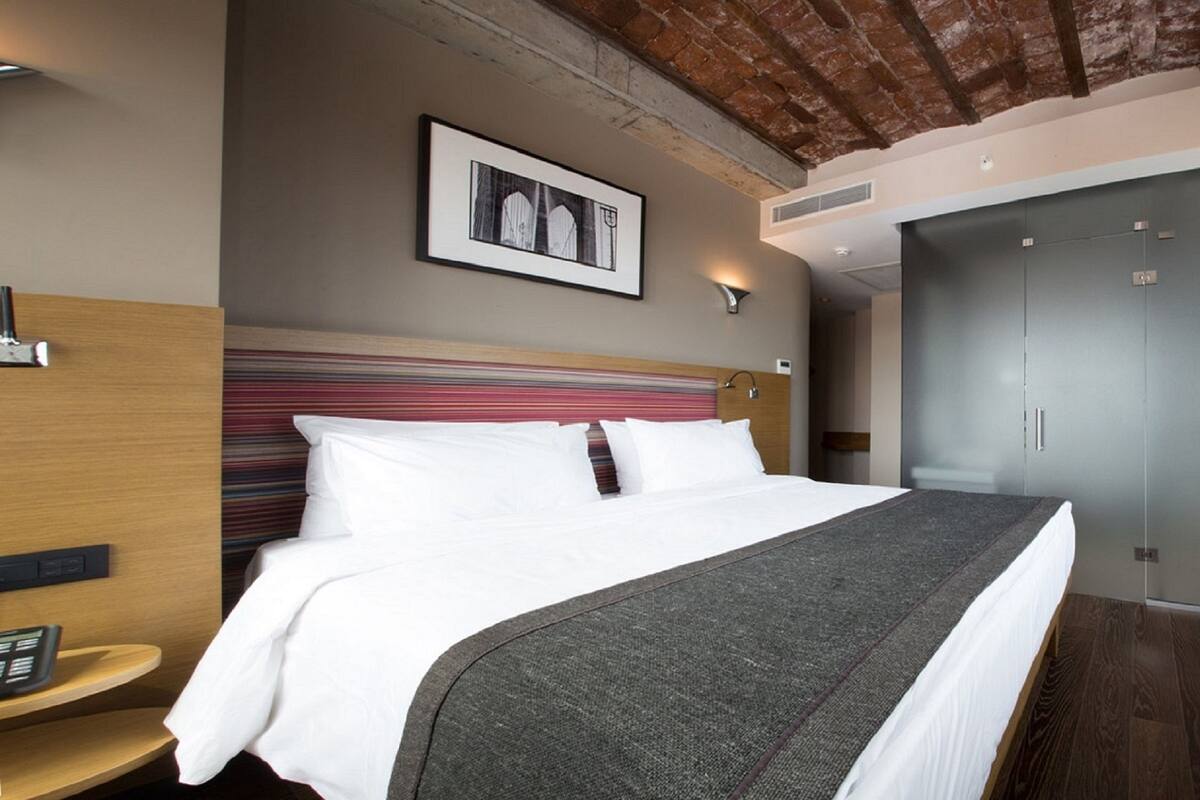 Une chambre d’hôtel avec un lit, un bureau sur lequel se trouve un panier de fruits, une armoire et un tableau encadré au mur.