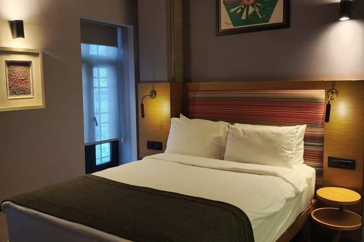 Un lit bien fait, recouvert d’une couverture verte, avec une tête de lit en bois et une petite table ronde placée à côté.