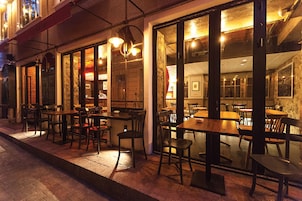 An outdoor dining area with tables and chairs, large windows, and a brick wall.