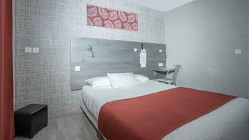 Ein modernes Schlafzimmer mit Bett, roter Decke, Kopfteil, Wandlampe und einem kleinen Tisch.