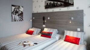 A bedroom with two beds, a cityscape painting, and a wooden headboard. - Hotel Mac Bed (Poitiers)