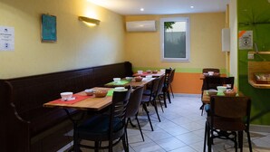 A restaurant with a long counter, multiple chairs, and a bench. There are tables with bowls and baskets, and a window with a view. - Hotel Mac Bed (Poitiers)