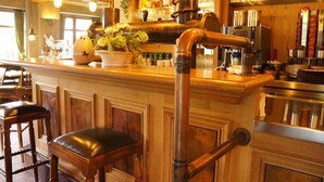 A bar area with wooden paneling, a copper pipe, bar stools, and a potted plant. - Hotel Traube (Loef)