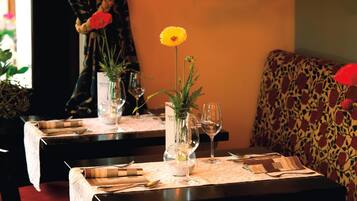 Een eettafel gedekt met wijnglazen, bestek en een vaas met een gele bloem.