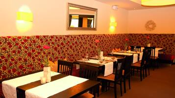 A restaurant with tables set for dining, a mirror on the wall, and a patterned wallpaper.