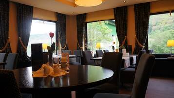 A dining area with a round table, chairs, and a view of greenery outside.