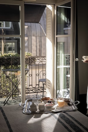 A breakfast tray with a teapot, cup, bowl of berries, croissant, and a jug of juice on a balcony with a view of a building and a metal railing. - Hotel Bachaumont (Paris)