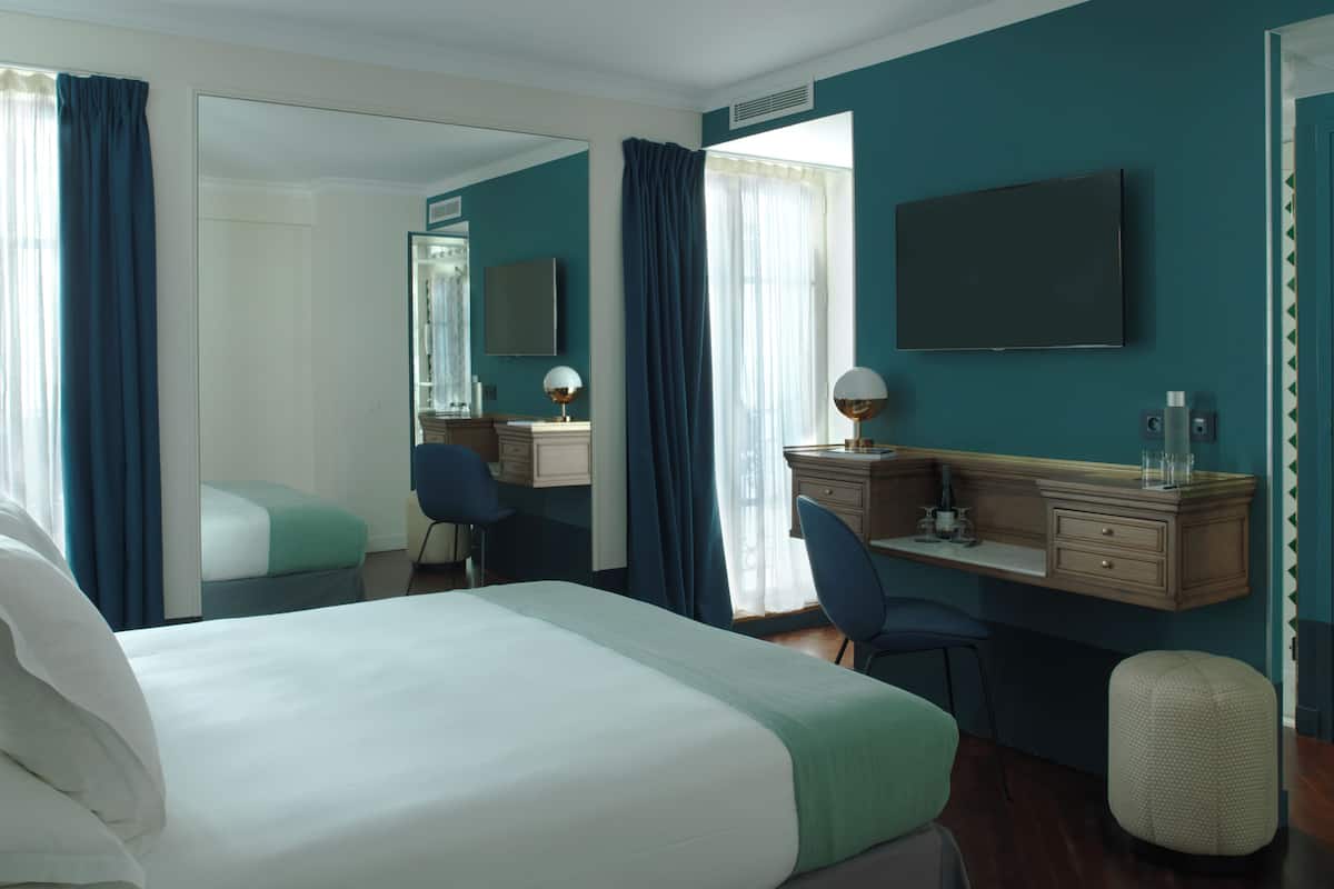 A hotel room with a bed, a desk, a chair, a mirror, and a TV.