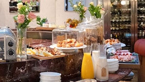 A breakfast buffet with various food items, a juice dispenser, and a wine cooler in the background. - Hotel Bachaumont (Paris)