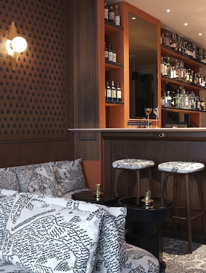 A bar area with shelves of liquor bottles, a mirrored bar counter, and a seating area with patterned cushions.