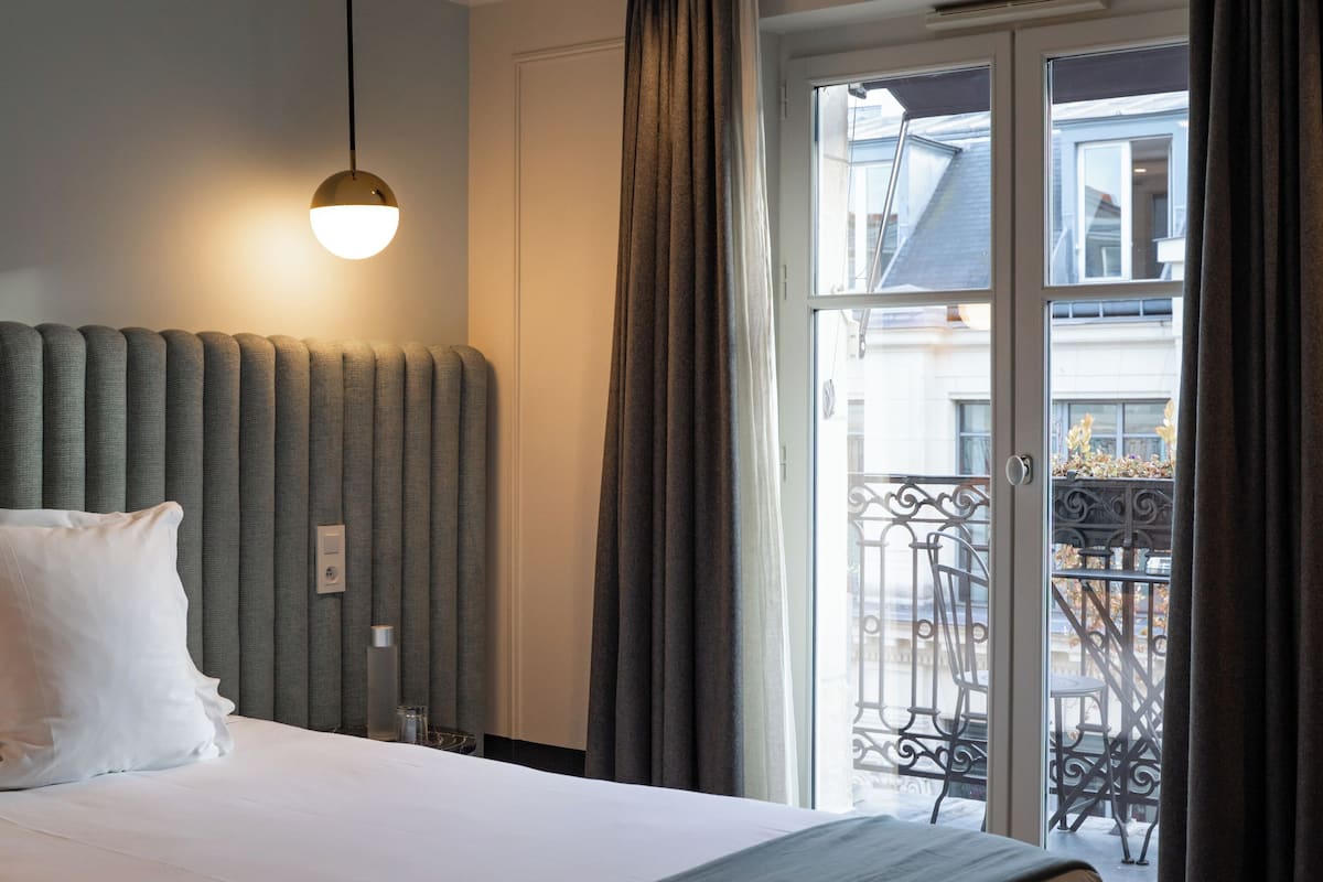 A hotel room with a large bed, a headboard, a bedside table, a lamp, and a view of the outside balcony.