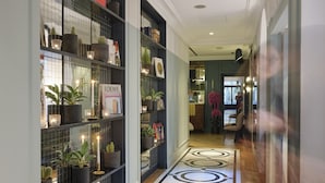 A hallway with a patterned floor, shelves with plants and books, and a 'LODEWE' sign. - Hotel Bachaumont (Paris)