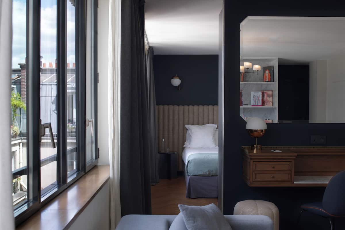 A hotel room with a large window, a bed, a desk, and a chair.