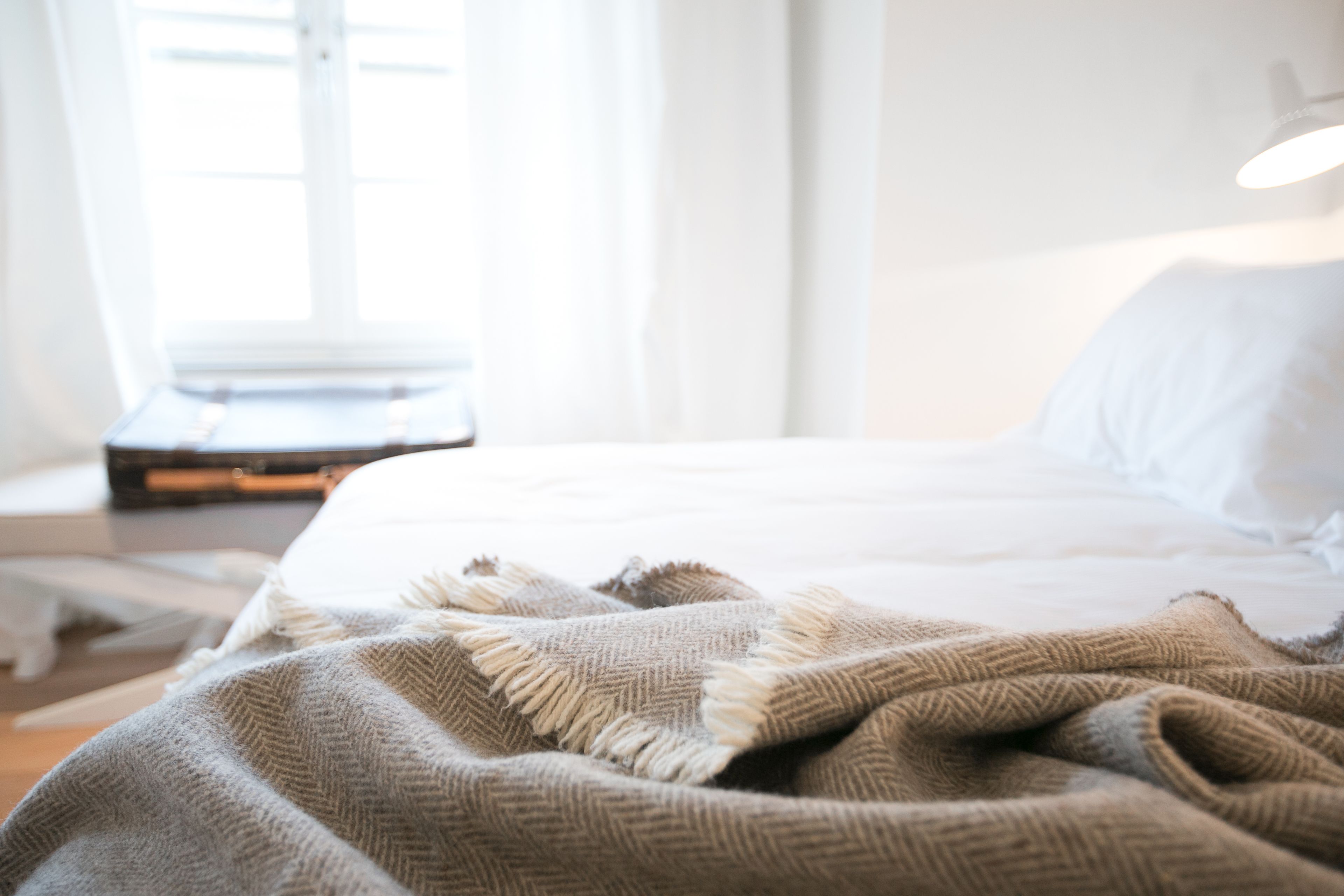 A neatly made bed with a white comforter and a beige blanket.