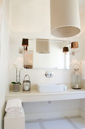 Un baño moderno con un espejo grande, dos lámparas de pared, un lavamanos y una pila de toallas.