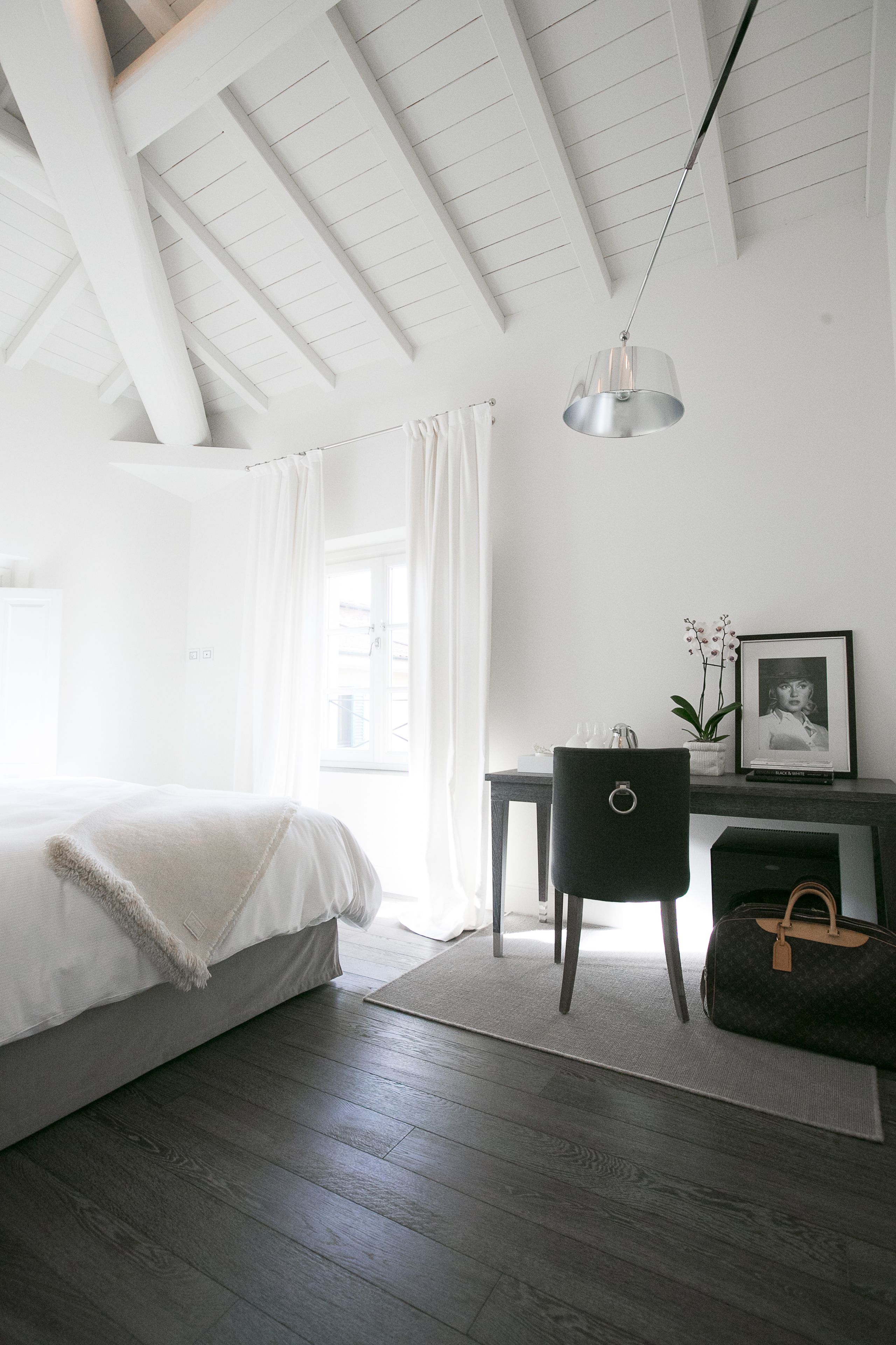 A bedroom with a bed, a desk, a chair, a lamp, and a suitcase.