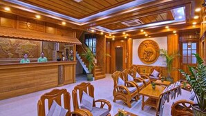 A wooden interior with a reception desk, seating area, and a large wall clock. - Hotel Dingar (Mandalay)