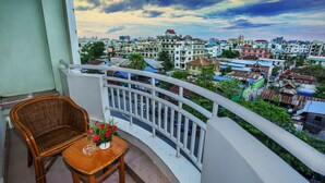 A balcony with a wicker chair and a small table with a vase of flowers. - Hotel Dingar (Mandalay)