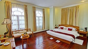A hotel room with a large bed, a desk with a chair, a small table with a bowl of fruit, and a lamp. - Hotel Dingar (Mandalay)