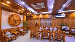 A hotel lobby with wooden furniture, a large emblem on the wall, and a television screen. - Hotel Dingar (Mandalay)