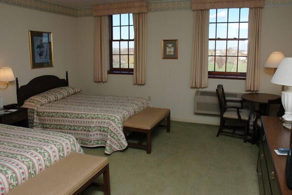 A room with two beds, a desk, a chair, and two windows with curtains.