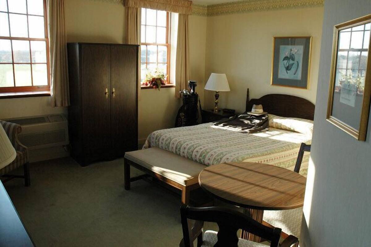 A bedroom with a bed, a wooden desk, a chair, a wardrobe, and a window with curtains.