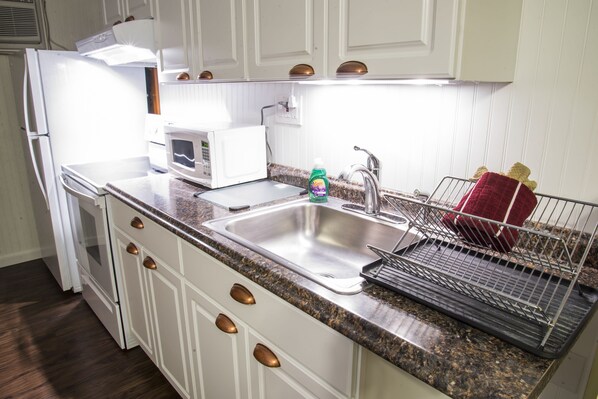 A kitchen with white cabinets, a stainless steel sink, a microwave, and a dish rack.