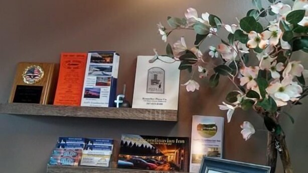 A reception area with a marble counter, a hanging pendant light, a framed menu, and a potted plant with white flowers. - Fairway Overnight & Extended Stay (Manchester)